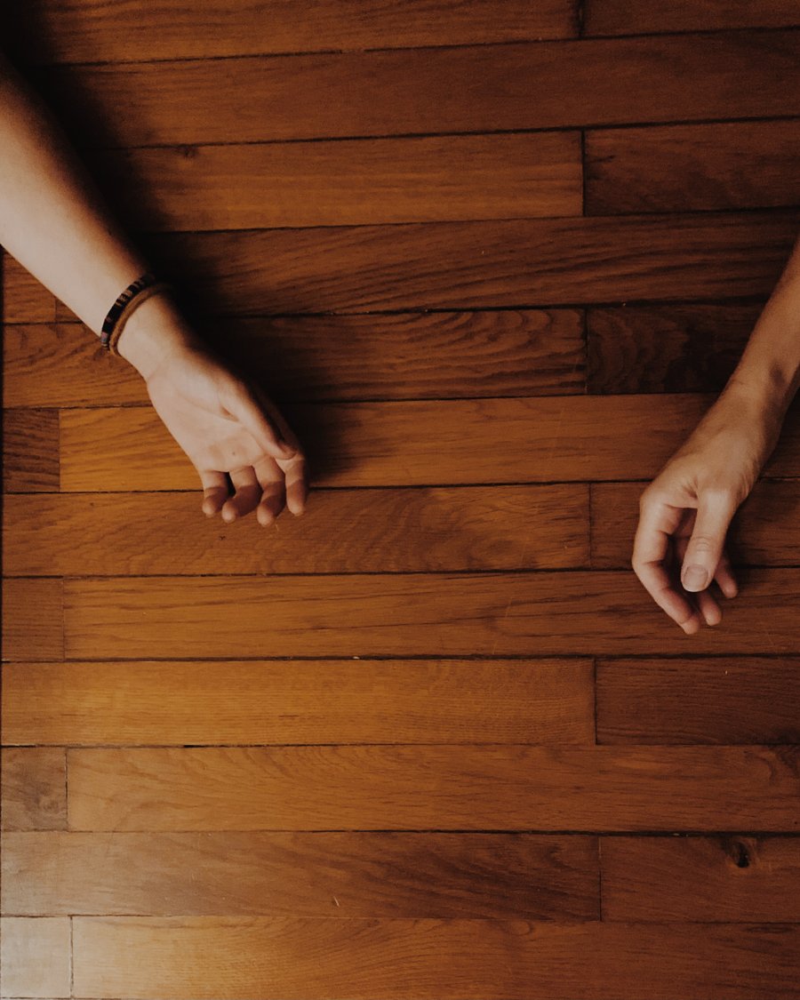 Mains posées sur le parquet, à côté d'un tapis de yoga